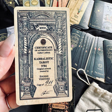 Load image into Gallery viewer, Hand holding the "Kabbalistic Tarot 5781" certificate of authenticity card in front of a fanned spread of Hebrew-lettered tarot cards, with the branded deck box and drawstring bag visible below - Let's Jam collection