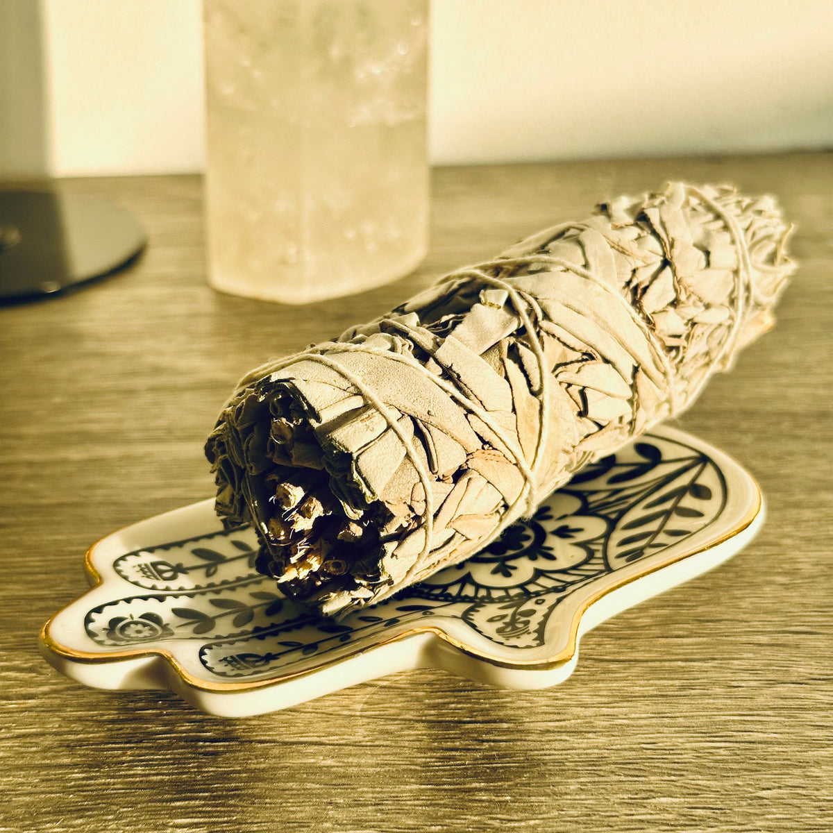 White sage smudge stick resting on a decorative ceramic leaf-shaped dish, on a wooden surface with a crystal in the background - Let's Jam smudge collection