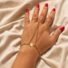 Load image into Gallery viewer, Close-up of a gold sun hand chain bracelet with a delicate finger ring and fine chains, worn on a hand with red nails against soft cream fabric.