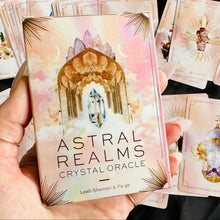Load image into Gallery viewer, Hand holding the Astral Realms Crystal Oracle deck box with pastel crystal and gemstone illustrated cards fanned out on black fabric - Let's Jam collection