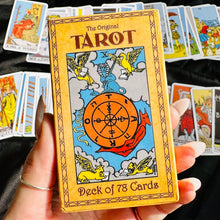 Load image into Gallery viewer, Hand holding "The Original Tarot" deck box featuring the Wheel of Fortune wheel and geometric star illustration, in front of a fanned spread of classic Rider-Waite-style tarot cards - Let's Jam collection