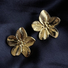 Load image into Gallery viewer, Pair of gold-plated stainless steel flora flower stud earrings with textured petal detailing, laid on dark navy fabric - Let's Jam jewellery collection