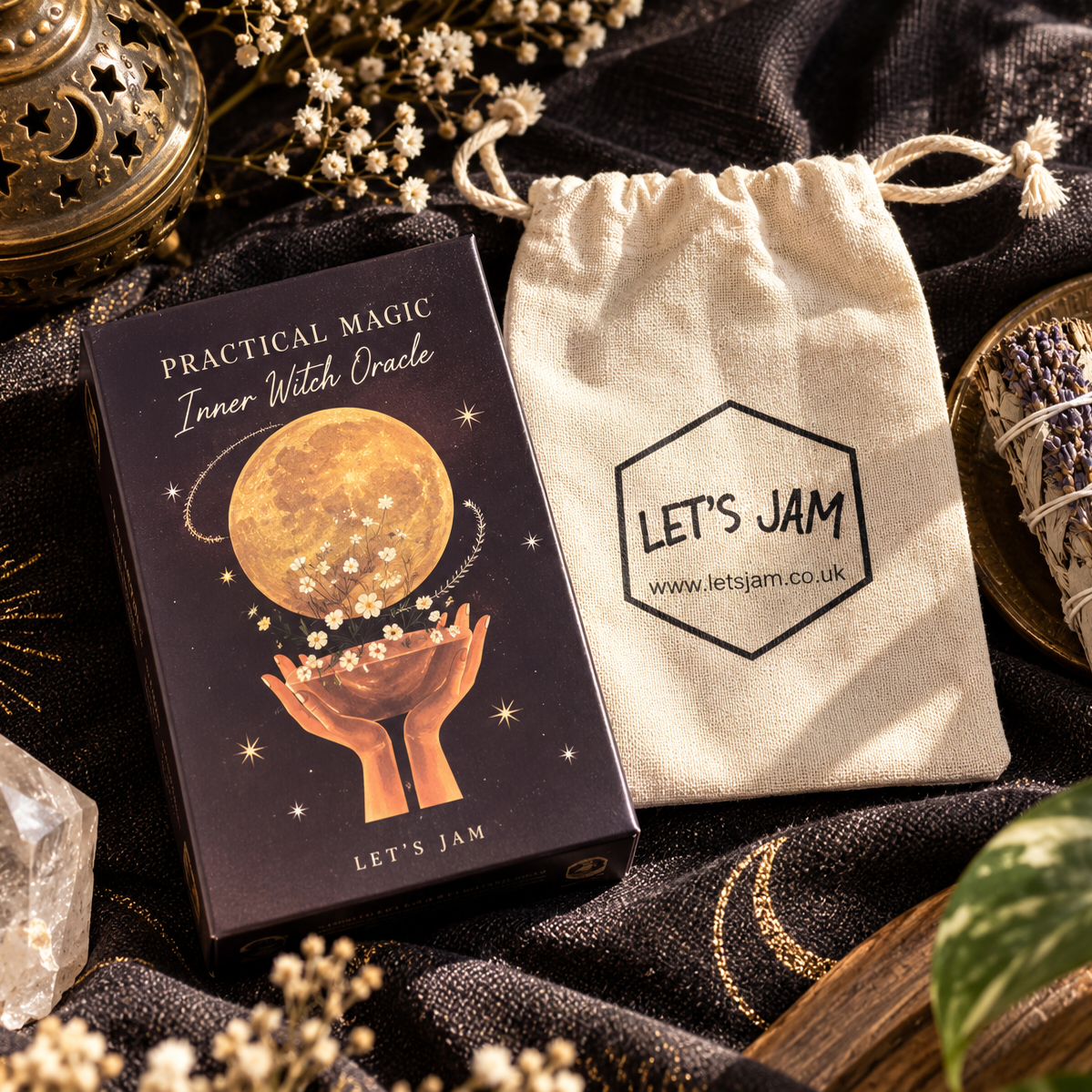 Inner Witch Oracle card deck box by Let's Jam next to its beige drawstring bag, styled with crystals, dried flowers, and a sage bundle on a dark patterned fabric background.
