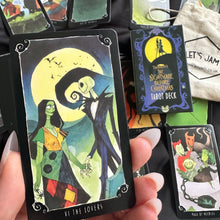Load image into Gallery viewer, Hand holding a "The Lovers" tarot card illustrated with Jack and Sally from The Nightmare Before Christmas under a full moon, with the branded deck box and fanned spooky-themed cards visible in the background - Let's Jam collection