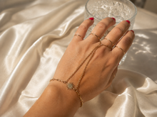 Load image into Gallery viewer, Close-up of a gold sun hand chain bracelet with a delicate finger ring and fine chains, worn on a hand with red nails against soft cream fabric.