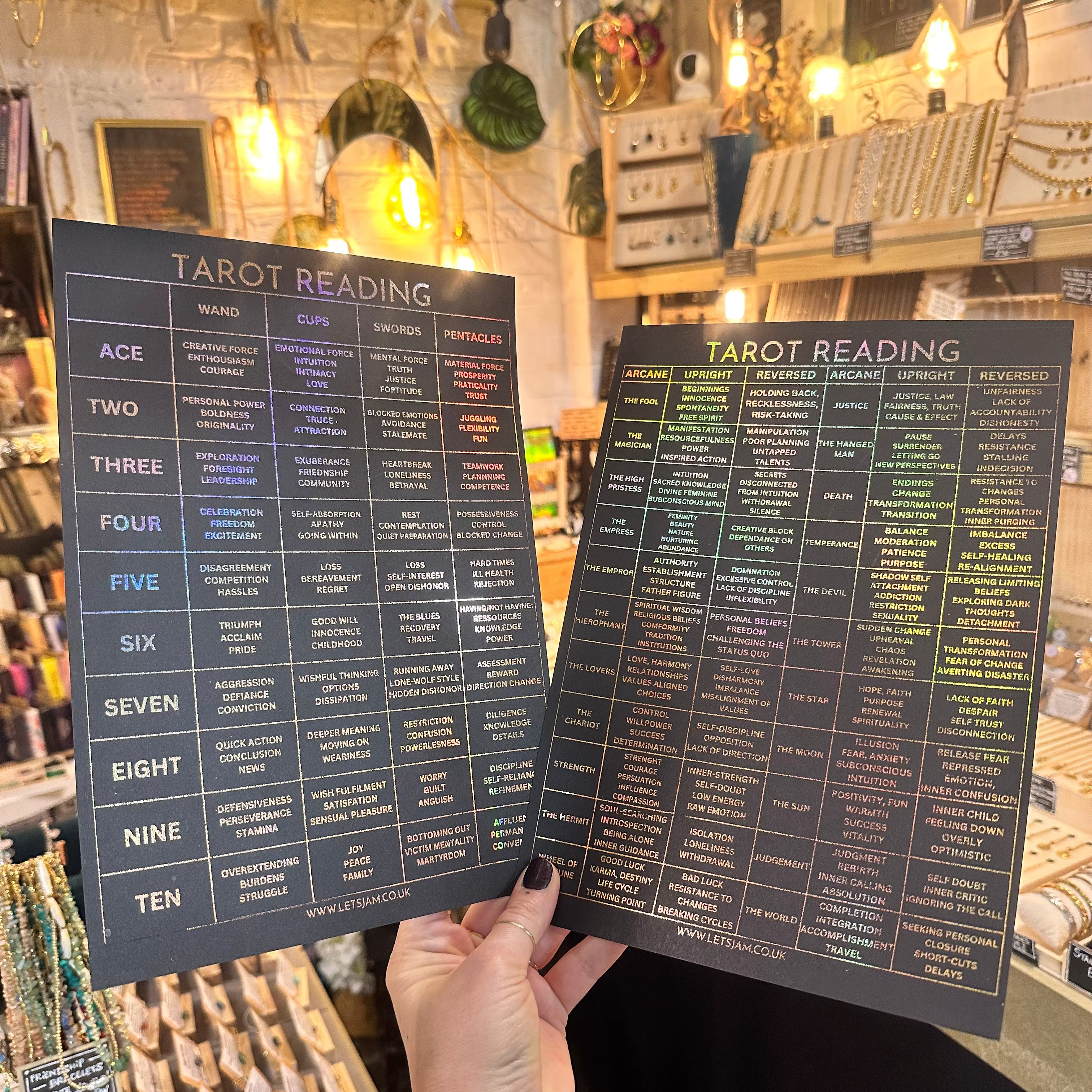 Hand holding a black holographic rainbow tarot reading chart poster with gold and colourful text, shown in a boho shop setting - Let's Jam print collection