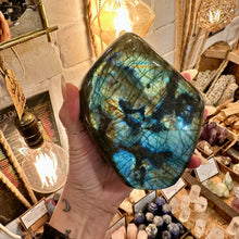 Load image into Gallery viewer, Hand holding a large polished labradorite freeform, blue flash over darker inclusions - Let's Jam, Camden Town