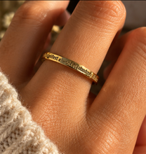 Load image into Gallery viewer, A close-up of a hand wearing a thin gold ring engraved with the phrase 'I manifest a world of abundance & kindness'.
