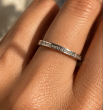 Load image into Gallery viewer, A close-up of a silver band ring worn on a finger, engraved with the phrase 'I manifest a world of abundance & kindness'.