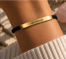 Load image into Gallery viewer, Gold I Am Enough bar on a black braided cord bracelet, worn - Let's Jam, Camden Town London