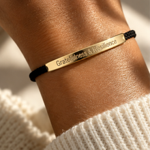Load image into Gallery viewer, Black cord bracelet with a gold engraved bar in warm sunlight - Let's Jam, Camden Market