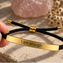 Load image into Gallery viewer, Black cord bracelet with a gold I Am Enough plate beside dried flowers - Let's Jam jewellery, Camden Town