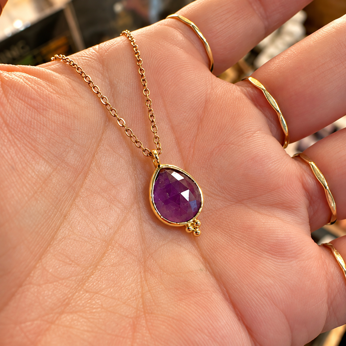 Faceted purple amethyst tear drop pendant in a gold setting held in the hand - Let's Jam, Camden Market