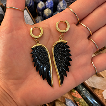 Load image into Gallery viewer, Pair of black angel wing earrings on gold clip hoops held in the hand - Let's Jam, Camden Market, London