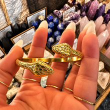 Load image into Gallery viewer, Gold snake cuff with a snake head at each end held in the hand - Let's Jam jewellery, Camden Market, London