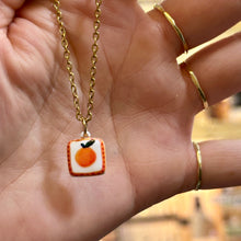 Load image into Gallery viewer, Orange ceramic pendant on a gold chain held in the hand - Let's Jam, Camden Market
