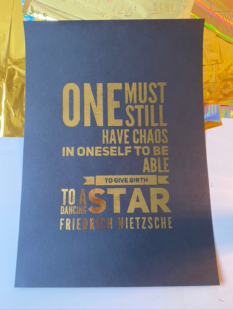 A gold print of a Friedrich Nietzsche quote about needing chaos within oneself to birth a dancing star, displayed on iridescent gift wrap - Let's Jam print collection