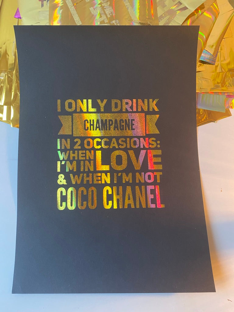 A black print with the Coco Chanel quote "I only drink champagne in 2 occasions: when I'm in love & when I'm not" in rainbow holographic lettering, beside iridescent gift wrap - Let's Jam print collection