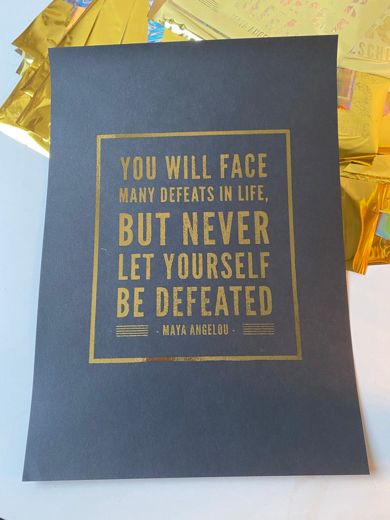 A black print with a gold-bordered quote by Maya Angelou about facing defeats but never being defeated, displayed on iridescent gift wrap - Let's Jam print collection