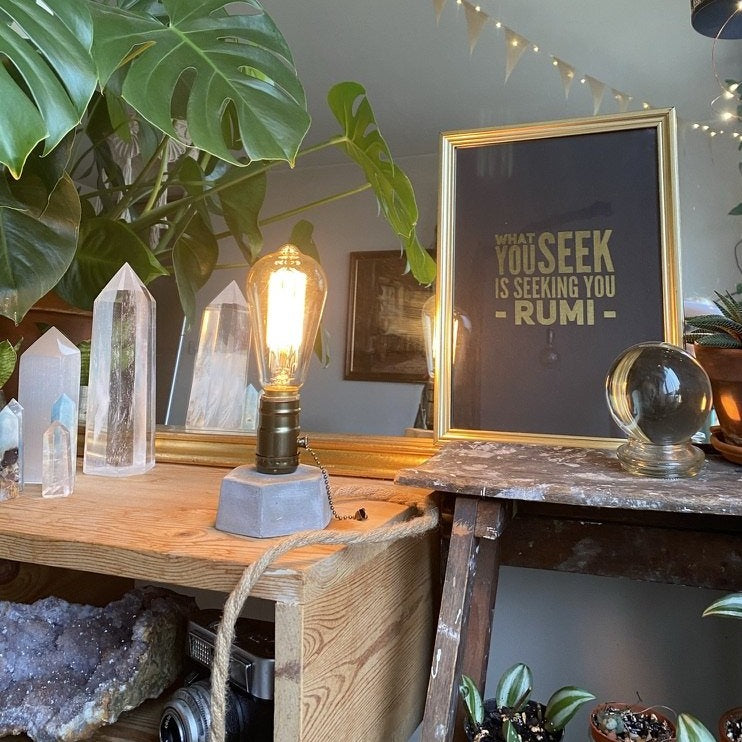 Hexagon concrete lamp with a glowing Edison-style filament bulb, displayed on a wooden shelf beside clear quartz crystal points and a gold-framed Rumi quote print - Let's Jam collection