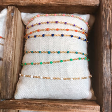Load image into Gallery viewer, A row of dainty gold-tone chain bracelets with small beaded accents in a range of colours, arranged on a textured cushion inside a wooden box - Let's Jam jewellery collection