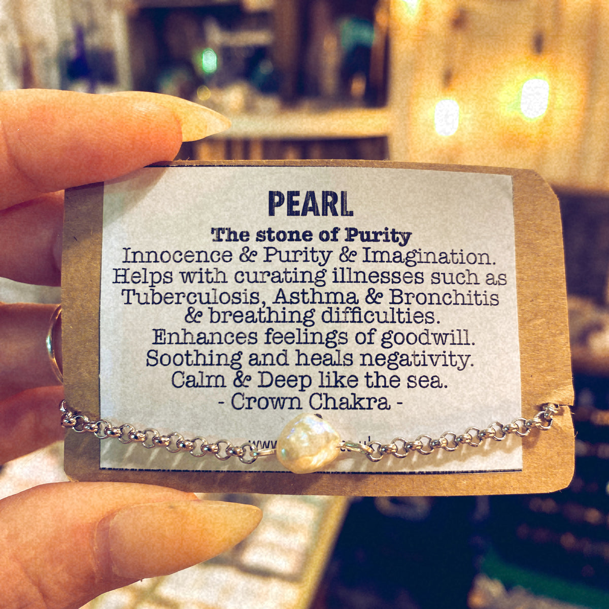 Handmade stainless steel bracelet with a real cultured white pearl charm, held alongside a printed card describing the stone's purity meaning - Let's Jam jewellery collection