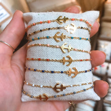 Load image into Gallery viewer, A row of gold-tone chain bracelets with anchor charms and colourful beaded accents, pinned to a cushion and held up to show the full collection of colours - Let's Jam jewellery collection