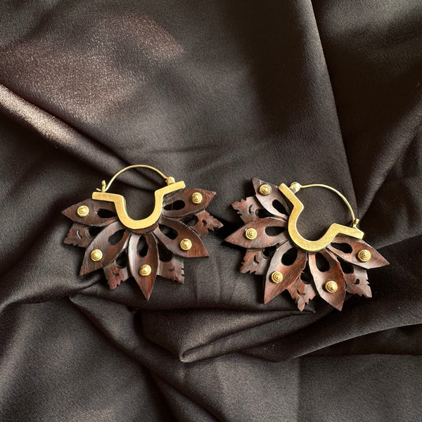 Pair of handcrafted brass hoop earrings with sculpted dark wood lotus flower petals riveted on, displayed on dark satin fabric - Let's Jam jewellery collection