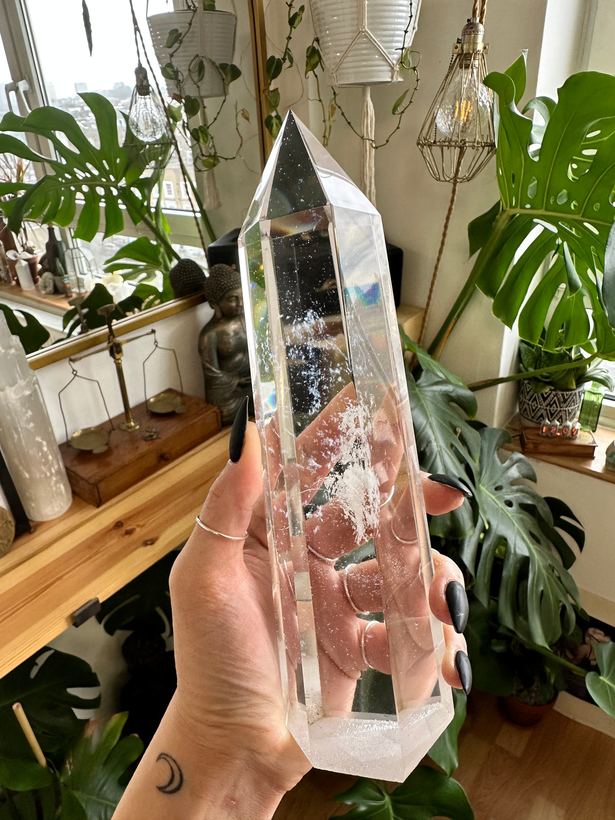 Hand holding a large clear quartz crystal tower point with natural internal inclusions, houseplants in the background - Let's Jam crystal collection
