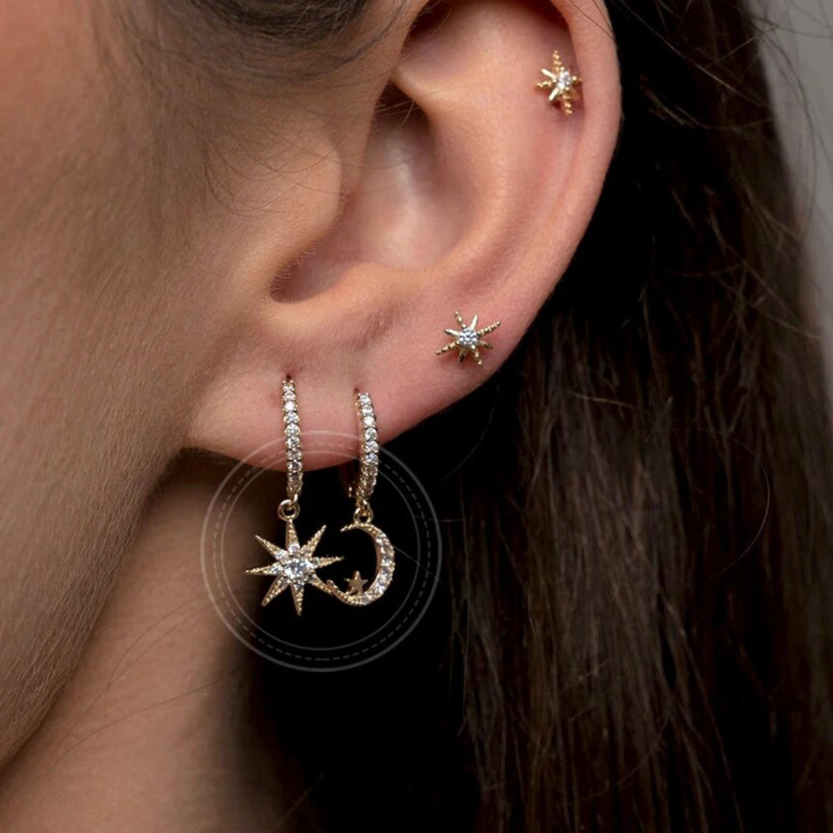 Close-up of a woman's ear styled with a gold-plated star stud earring in the cartilage and layered hoop drop earrings with star and crescent moon charms set with zirconia stones - Let's Jam jewellery collection
