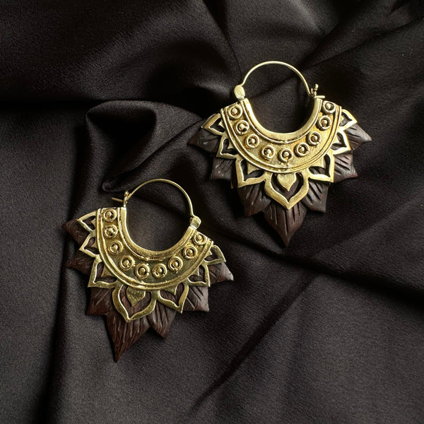 Pair of ornate gold-tone hoop earrings with an intricately carved dark wood lotus flower petal fringe, displayed on dark satin fabric - Let's Jam jewellery collection