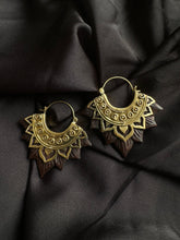 Load image into Gallery viewer, A pair of gold-colored brass earrings with a sculpted wood lotus flower design, displayed against a black fabric background.
