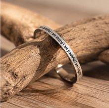 Load image into Gallery viewer, A silver band ring engraved with the words 'I am grateful | I am strong | I am powerful | I am happy' in a serif font, resting on a piece of driftwood over a wooden surface.
