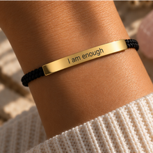Load image into Gallery viewer, Gold I Am Enough bar on a black braided cord bracelet, worn - Let's Jam, Camden Town London

