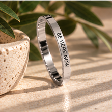 Load image into Gallery viewer, Silver 'Be here now' ring standing upright with green leaves behind - Let's Jam, Camden Market London
