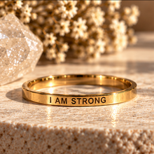 Load image into Gallery viewer, Gold affirmation ring engraved 'I am strong' on a stone surface - Let's Jam, Camden Market London
