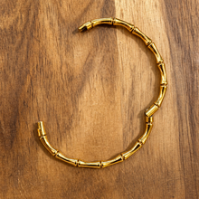 Load image into Gallery viewer, Gold bamboo bangle opened at its clip on wood - Let's Jam jewellery, Camden Market, London
