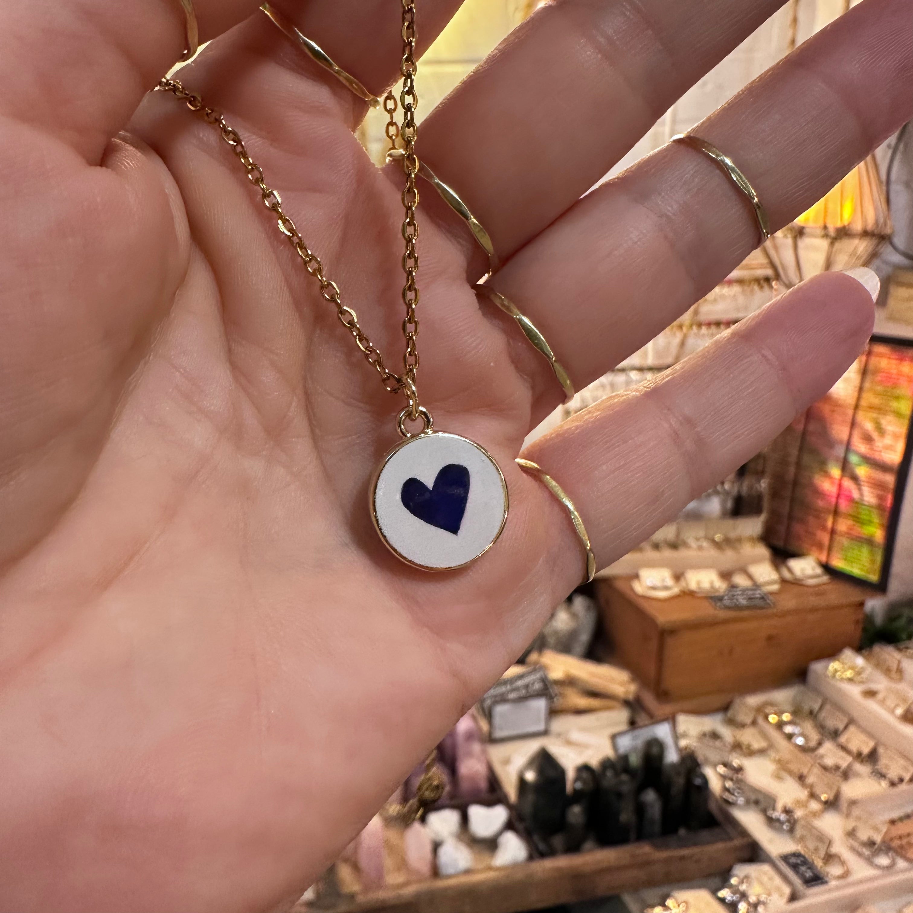 Round white ceramic pendant hand painted with a dark blue heart in the hand - Let's Jam, Camden Market, London
