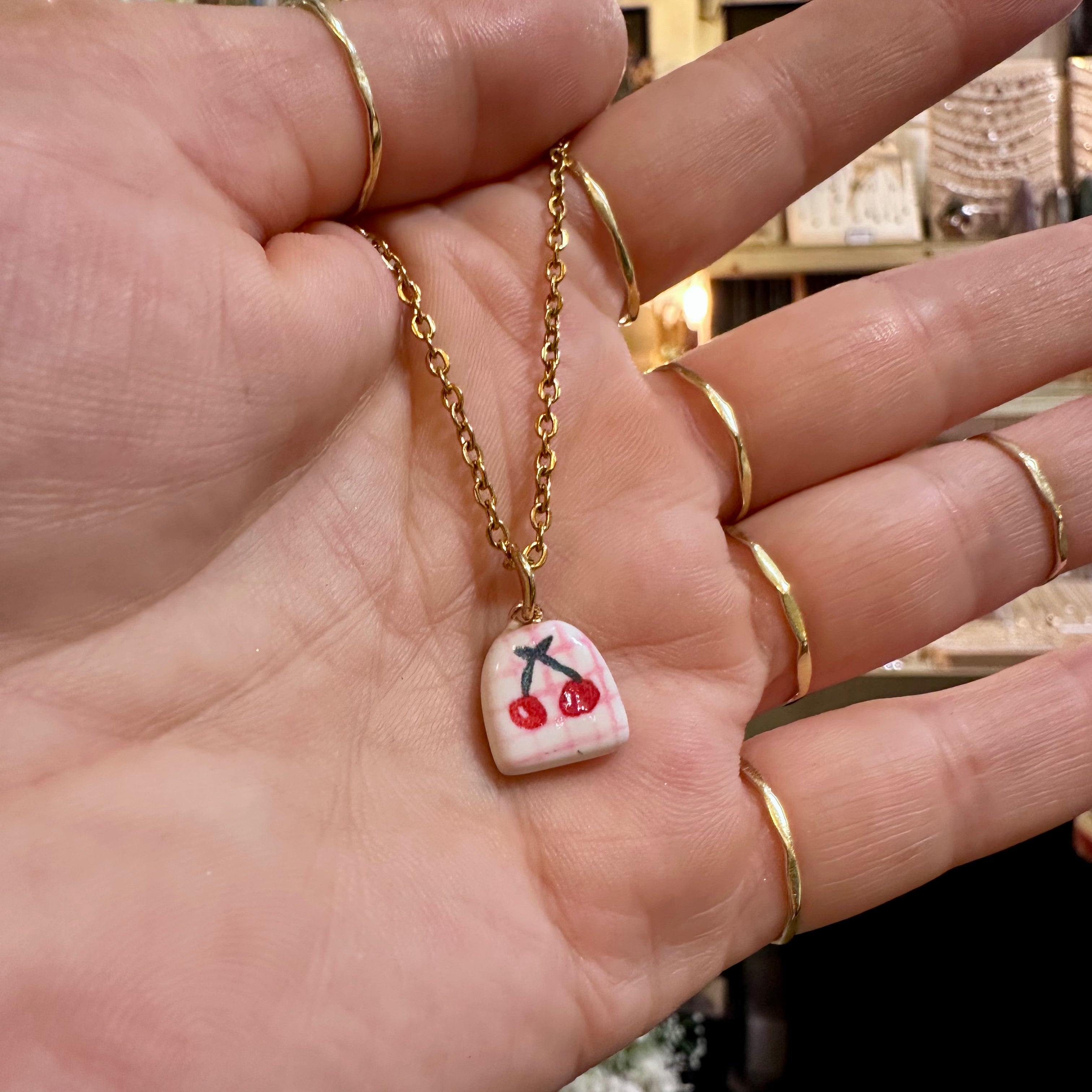 Cherry ceramic pendant on a gold chain held in the hand - Let's Jam, Camden Market