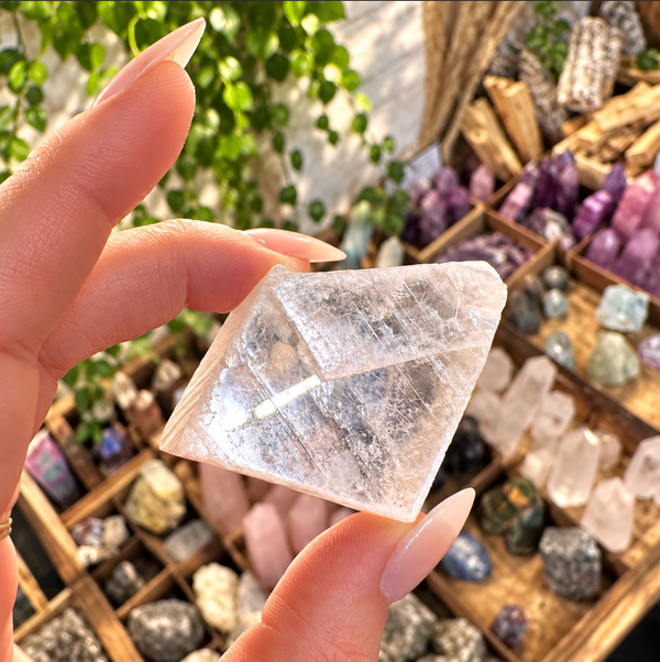 Clear calcite slab held between the fingers above a crystal display - Let's Jam, Camden Market