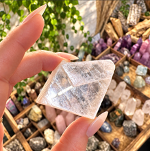 Load image into Gallery viewer, Clear calcite slab held between the fingers above a crystal display - Let's Jam, Camden Market
