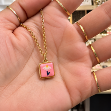 Load image into Gallery viewer, Pink daisy ceramic pendant on a gold chain held in the hand - Let's Jam, Camden Market London
