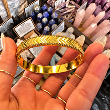 Load image into Gallery viewer, Gold arrow pattern bangle held in the hand - Let's Jam, Camden Market
