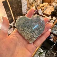 Load image into Gallery viewer, Moss agate crystal heart held up to show the green patterning running through it - Let's Jam, Camden Town
