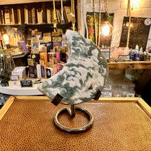 Load image into Gallery viewer, Moss agate crescent moon standing on its stand in the shop - Let's Jam, Camden Market
