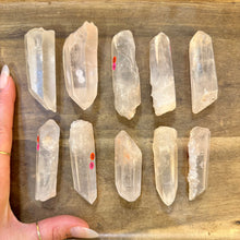 Load image into Gallery viewer, Ten raw clear quartz crystal points next to a hand to show their size - Let's Jam, Camden Market London
