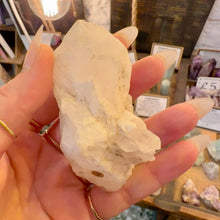 Load image into Gallery viewer, Raw milky quartz point held in the hand in the crystal shop - Let's Jam, Camden Town
