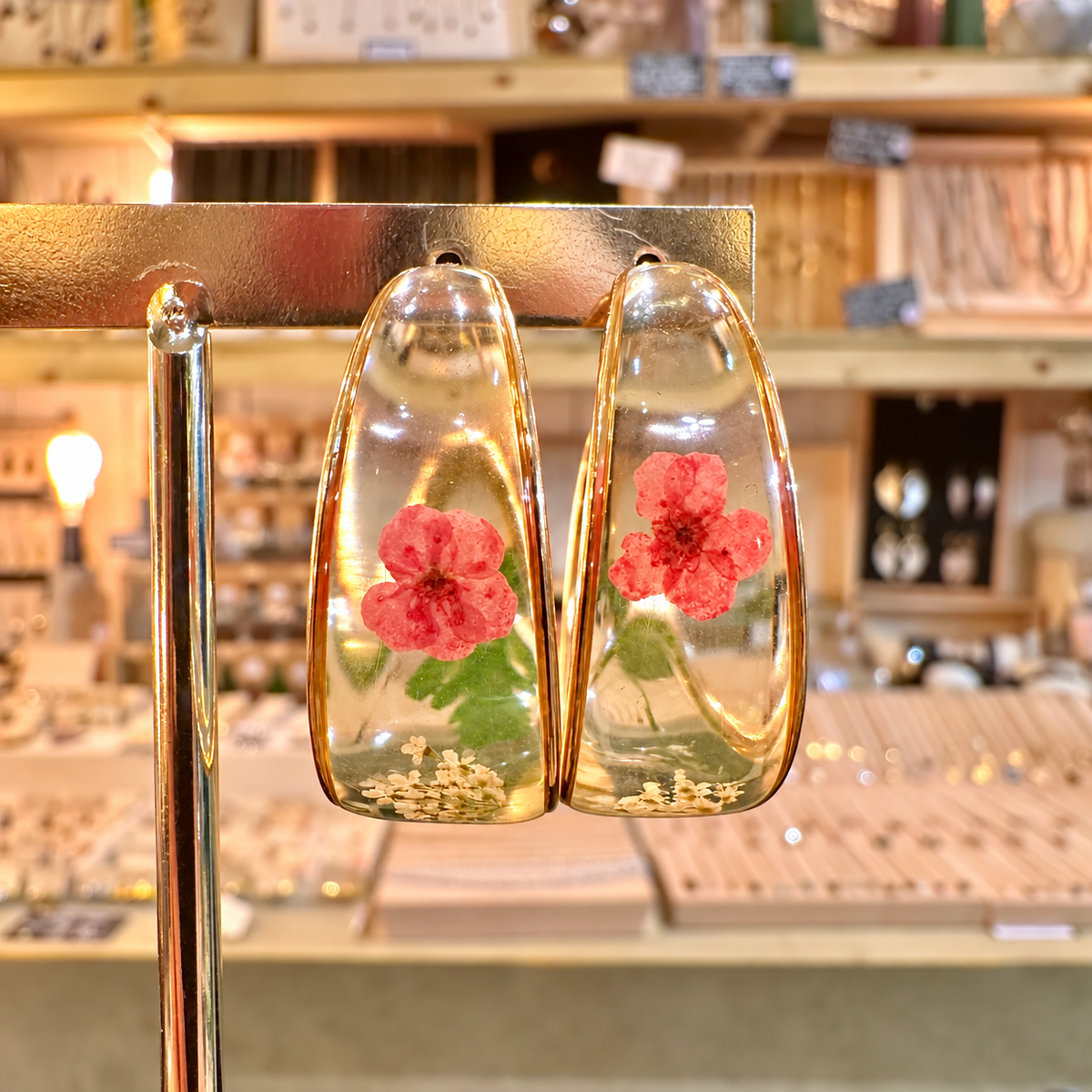 Chunky clear resin hoops with a real red flower and green leaves on a gold stand in the shop - Let's Jam, Camden Town London