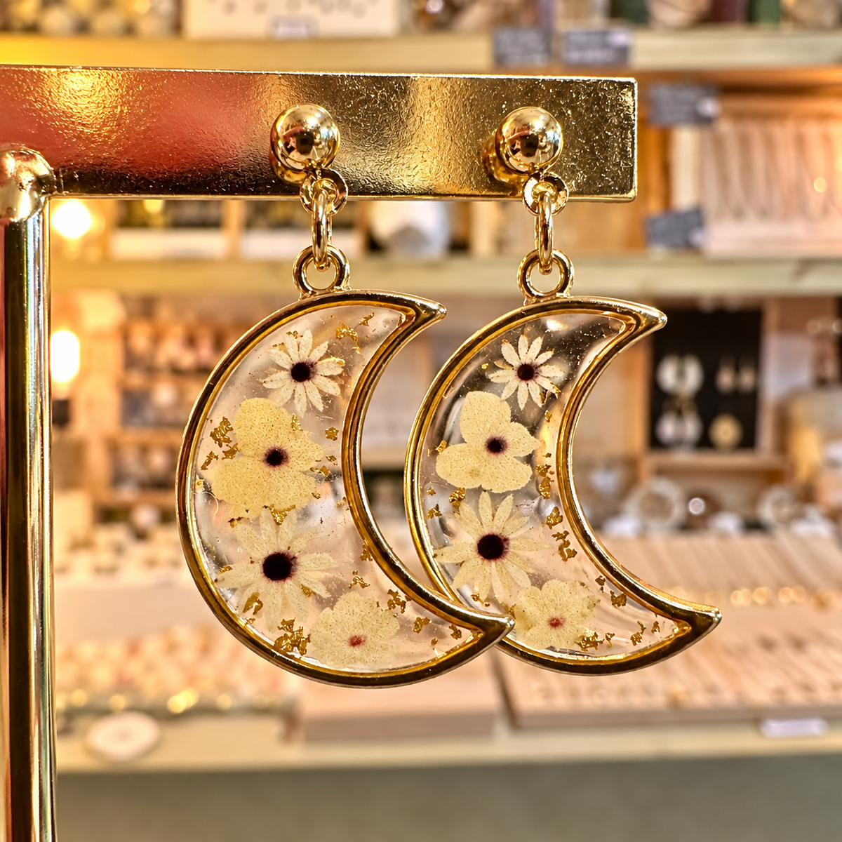 Crescent moon resin earrings filled with real white flowers on a gold stand in the shop - Let's Jam, Camden Market