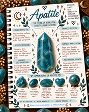 Load image into Gallery viewer, A spiral-bound notebook page featuring a decorative Apatite-themed inspirational poster with teal, gold, and white text, surrounded by illustrated leaves and several polished blue-green gemstones on a dark wood background.
